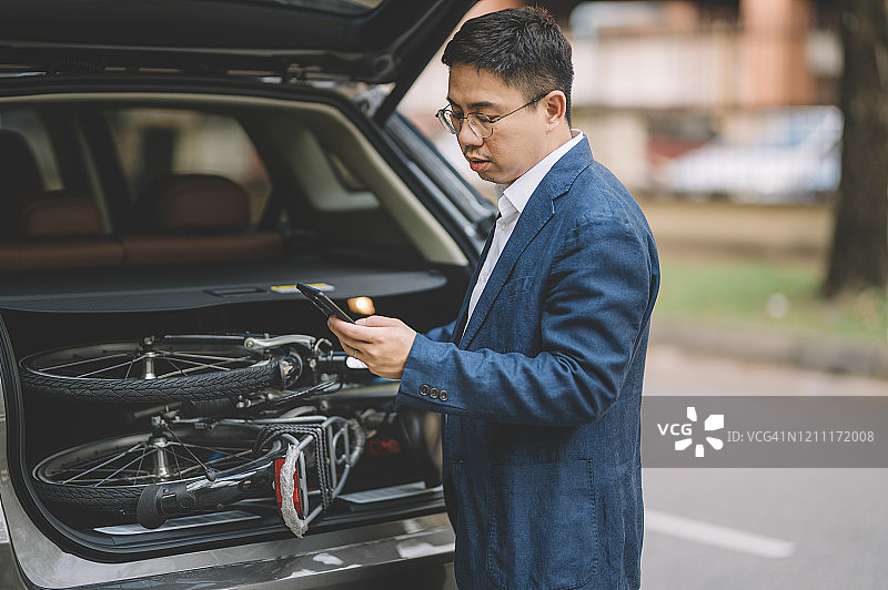 中国白领通勤，从车上卸下折叠自行车并回复手机信息图片素材