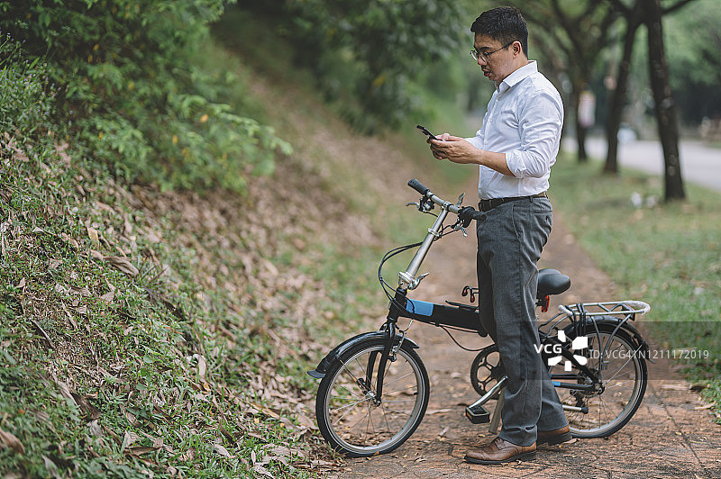 一名骑着折叠自行车通勤的华人白领行政人员在用手机回复消息图片素材