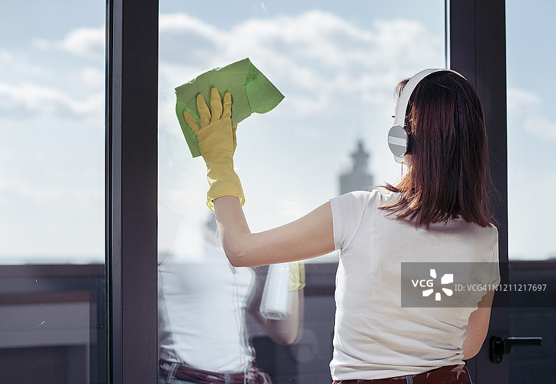 在现代客厅清洁窗户的年轻漂亮女人图片素材