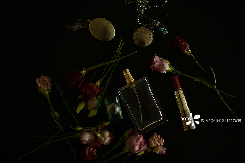 黑色背景上的粉色玫瑰、两瓶香水和两条项链图片素材