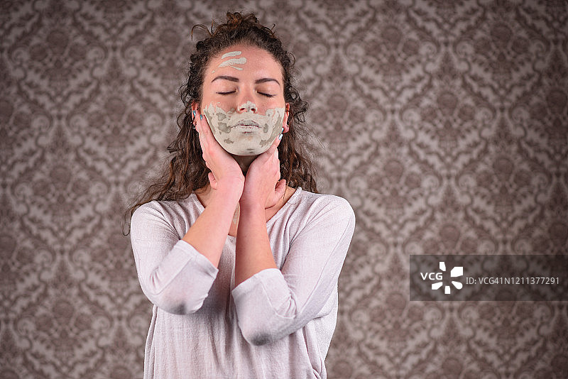 年轻漂亮女人敷泥膜触摸脸部的肖像图片素材
