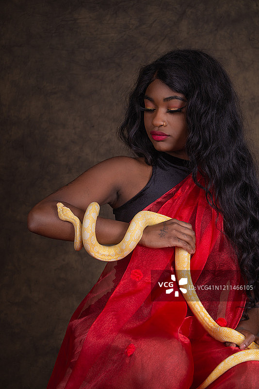 身穿红色面料的年轻黑人女性抱着黄色地毯蟒图片素材