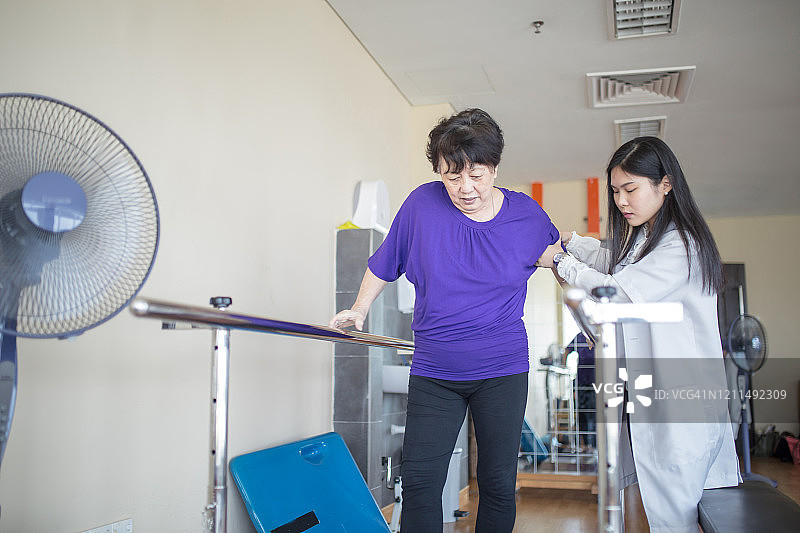 女理疗师帮助老年妇女在康复中心使用平行杆行走图片素材