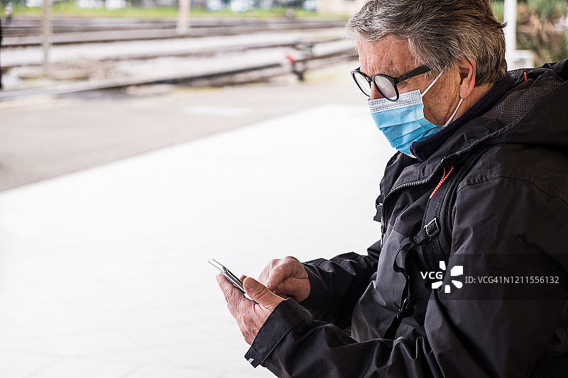 戴防护口罩使用智能手机的年长男人图片素材