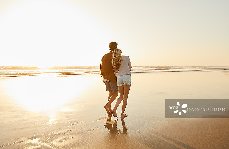 年轻夫妇在傍晚的海滩上散步图片素材