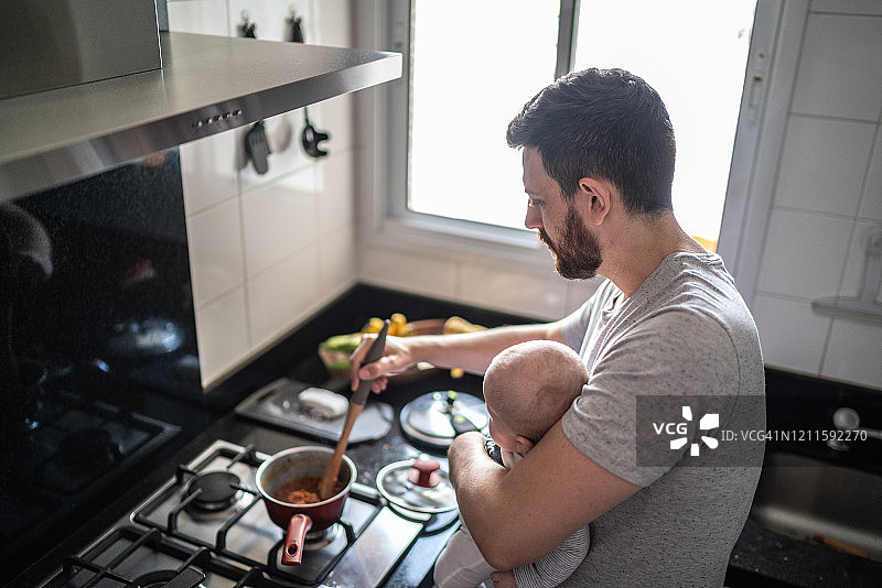 父亲和坐在腿上的儿子一起准备午餐图片素材