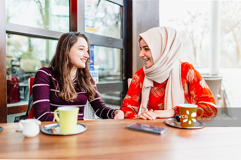 在咖啡店一起喝咖啡、谈笑风生的快乐年轻女性图片素材