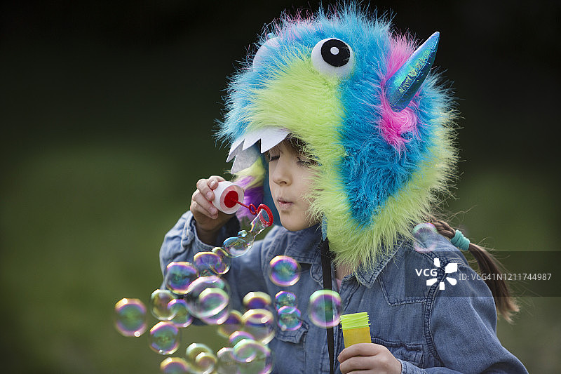 6-7岁的儿童吹泡泡，戴着怪物帽子图片素材