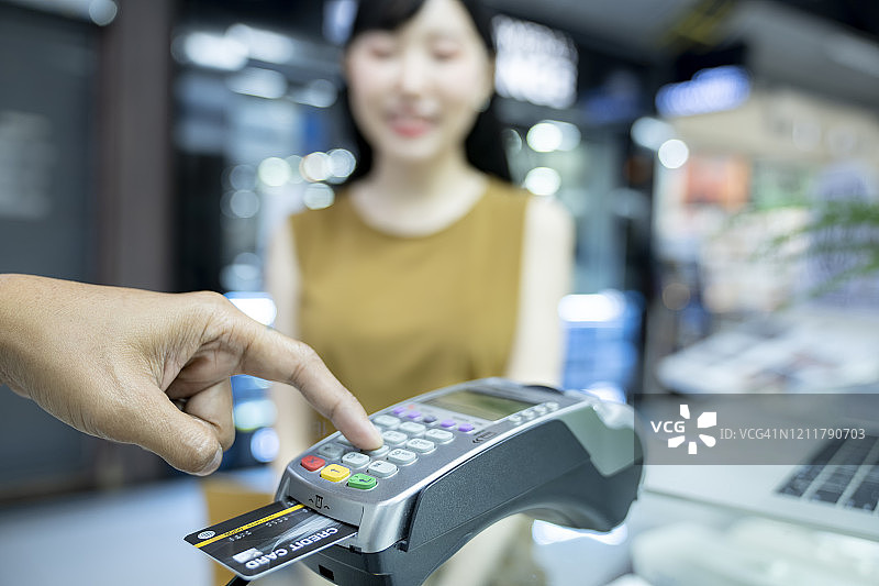 亚洲女子用信用卡通过读卡机支付购物款图片素材