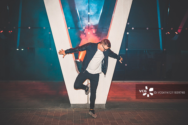 穿着皮夹克站在街上，手持烟雾弹的男人。手持蓝色烟雾弹的欧洲青少年的彩色肖像图片素材