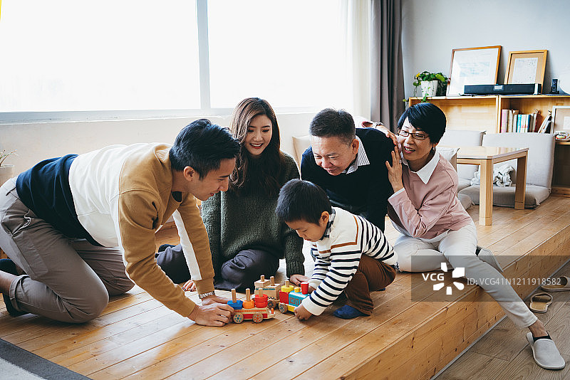 快乐的亚洲父母和祖父母坐在客厅的地板上，一起玩木制火车玩具图片素材