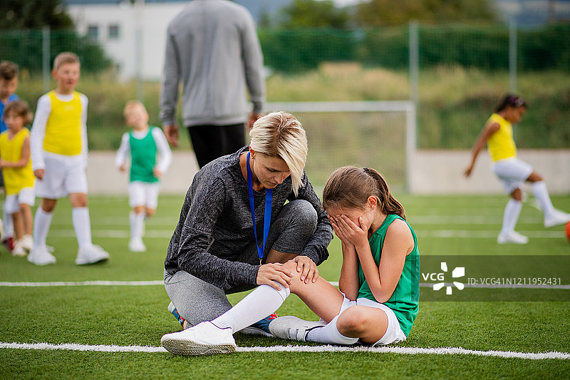 在足球场上，教练和受伤的哭泣小女孩图片素材