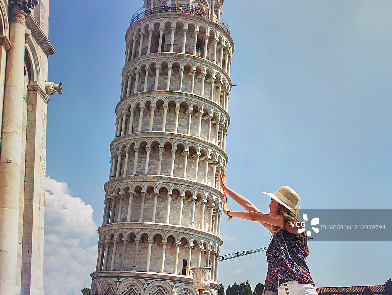戴着帽子，在意大利比萨斜塔前拍摄游客照的少女图片素材
