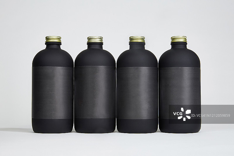 四个带黑色标签和金色瓶盖的16盎司哑光黑色瓶子图片素材