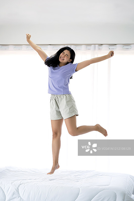 快乐的亚洲少女在床上跳跃时微笑。图片素材
