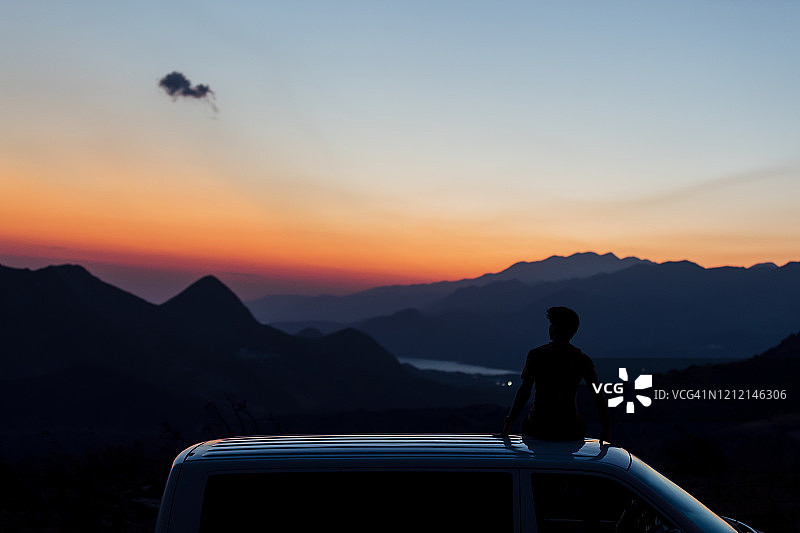 日落时分，男子坐在乡村货车顶上的剪影图片素材