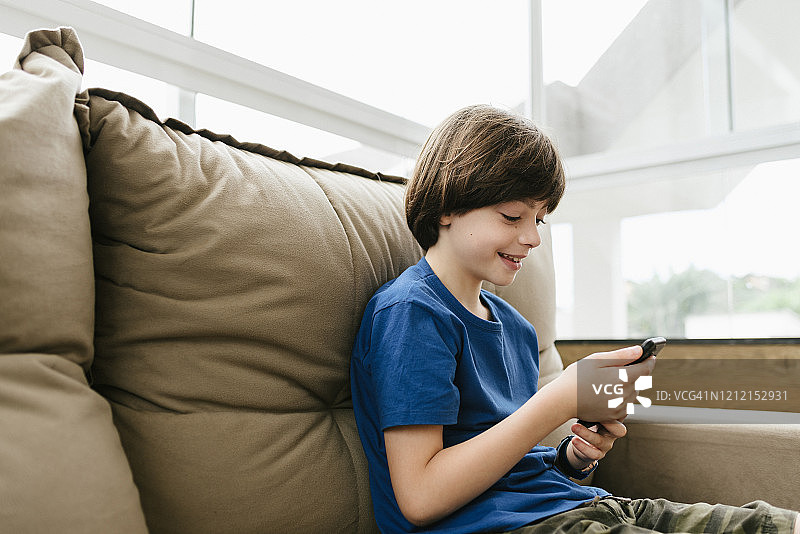 快乐的小男孩在沙发上玩手机图片素材
