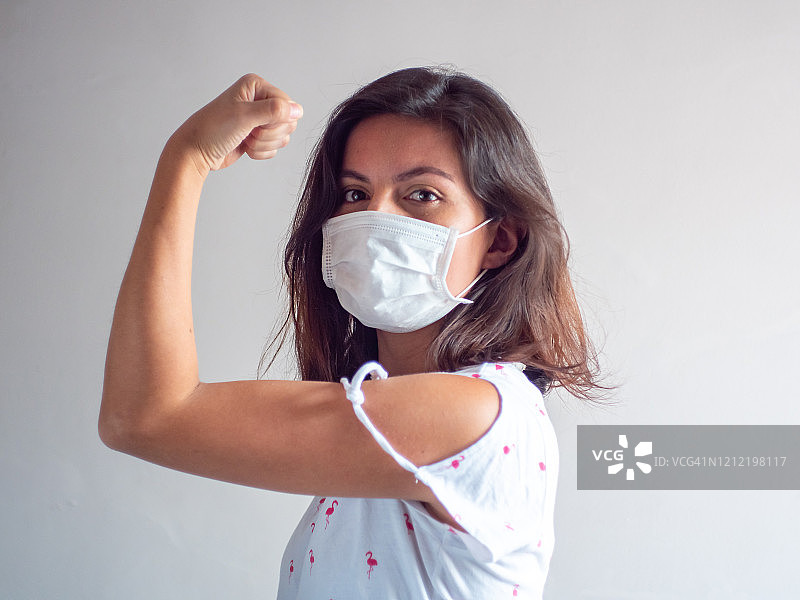 戴口罩的年轻西班牙裔女子展示手臂和拳头，预防咳嗽和流感病毒图片素材