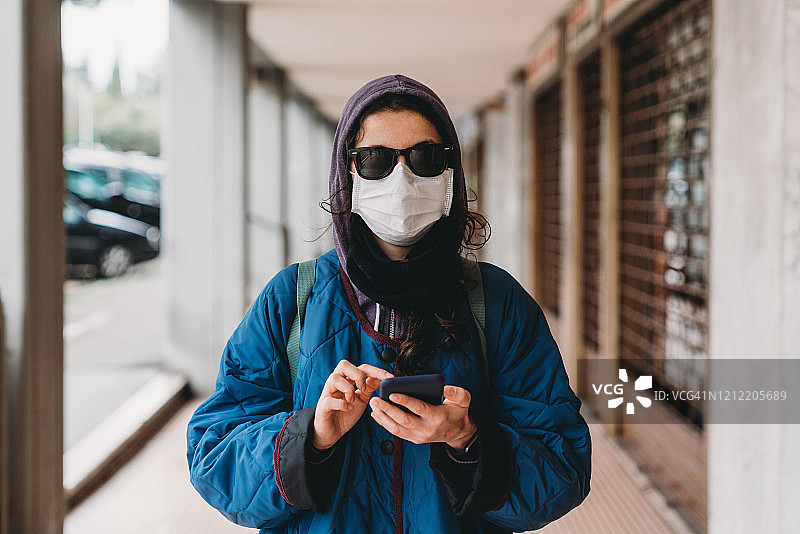 城市中戴口罩使用手机的年轻时尚女人肖像图片素材