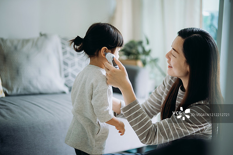 亚洲年轻母亲在客厅给女儿测体温。图片素材