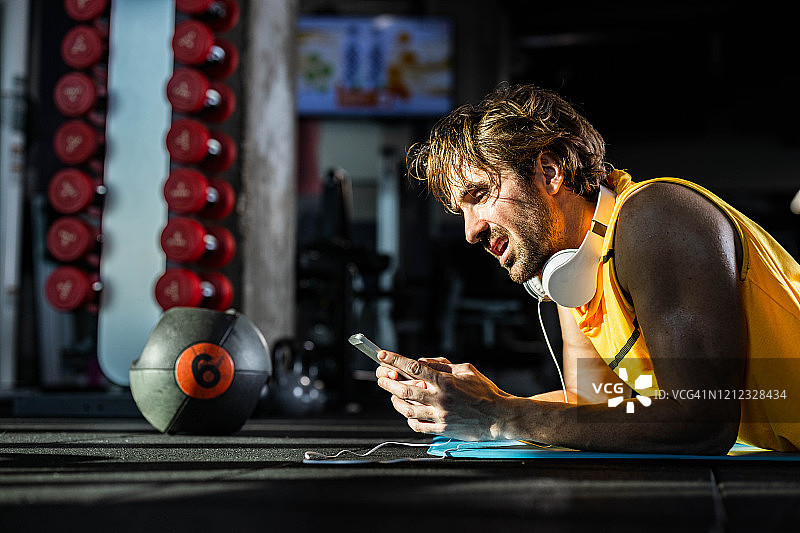 疲惫的运动 мужчина在健身房休息时使用手机。图片素材