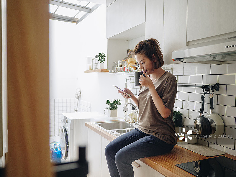 早上在厨房使用智能手机的年轻亚洲女性图片素材