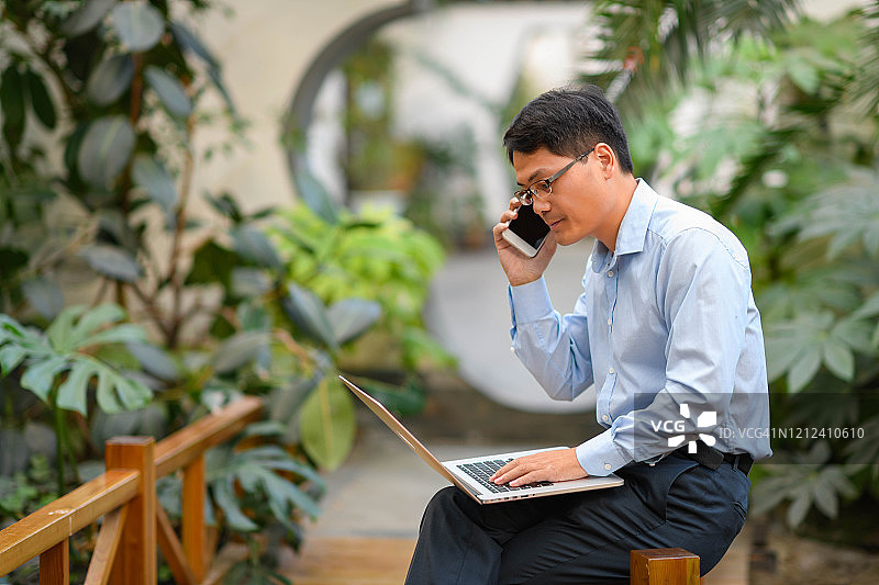 在花园里用电脑笔记本工作的亚洲商人图片素材