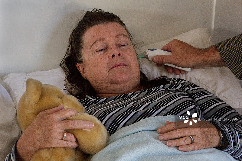 在家床上为生病的中年妇女测量耳温图片素材