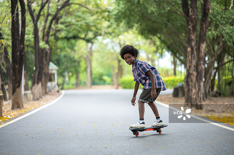 非裔美国男孩在公园的小路上玩滑板。男孩自学滑板。图片素材