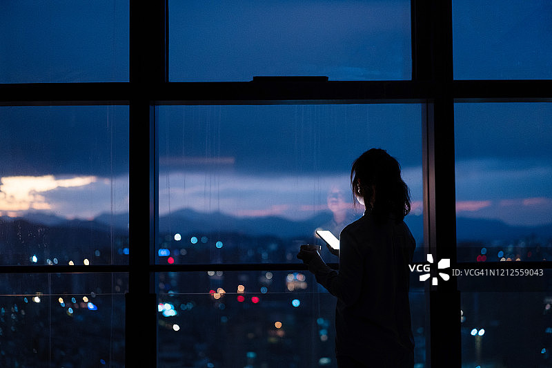 在家中窗边使用智能手机的亚洲女子图片素材