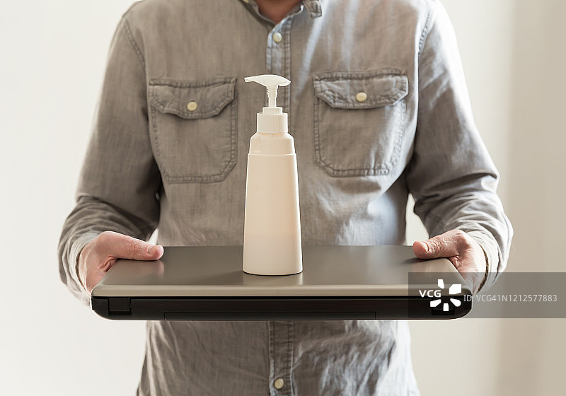 使用笔记本电脑和免洗洗手液的男人，工作场所和笔记本电脑上的免洗洗手液，个人卫生概念，手部消毒，病毒防护，疫情期间的远程工作图片素材