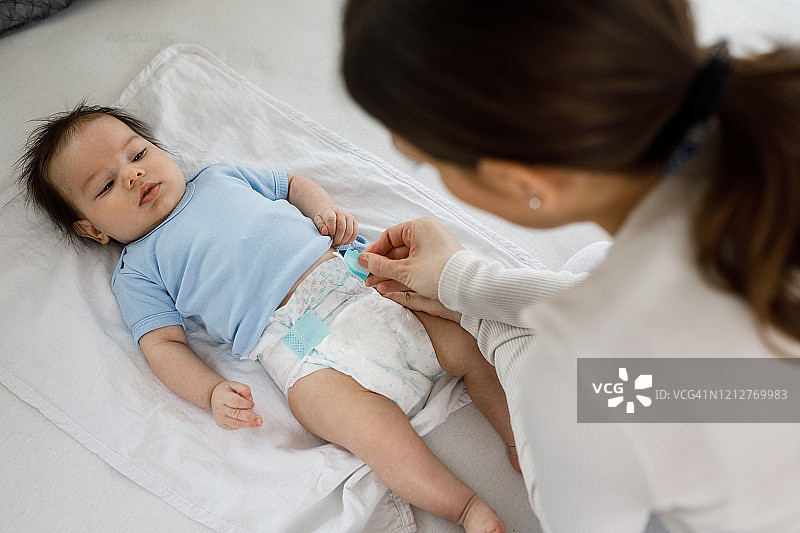 年轻妈妈在家为她的小男婴换尿布图片素材