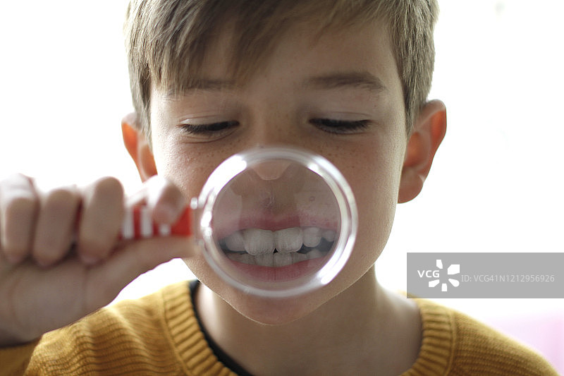 用放大镜观察牙齿的男孩图片素材