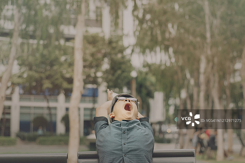 坐在公园长椅上打呵欠的青少年男子图片素材