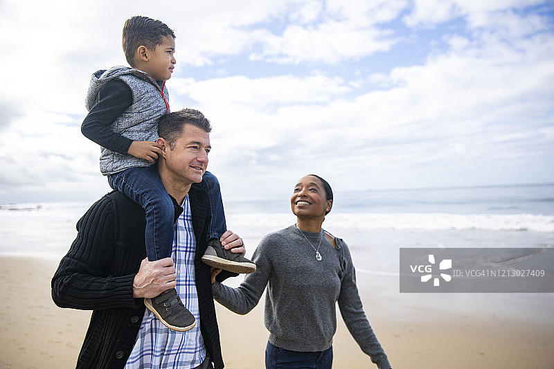 爸爸在沙滩上扛着蹒跚学步的孩子散步图片素材