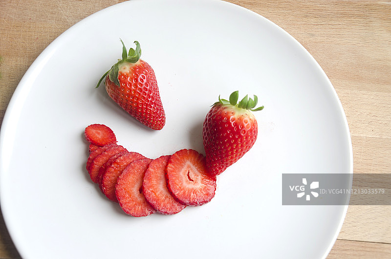 白色盘子上的两颗完整草莓和一颗草莓切片图片素材