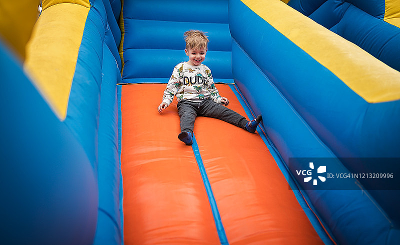快乐的小男孩在充气城堡上滑下来图片素材