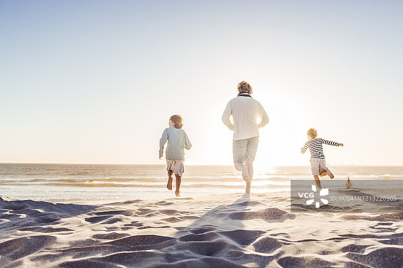 父亲在海滩上和儿子们玩耍，在沙滩上奔跑图片素材