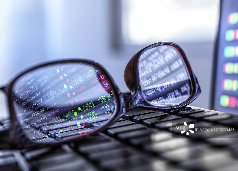 股票市场数据反映在笔记本电脑键盘上的眼镜中图片素材