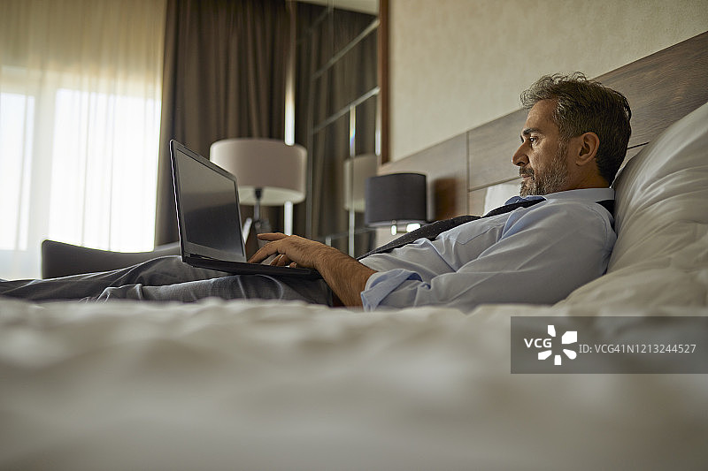 在酒店房间里躺在床上使用笔记本电脑的商人图片素材
