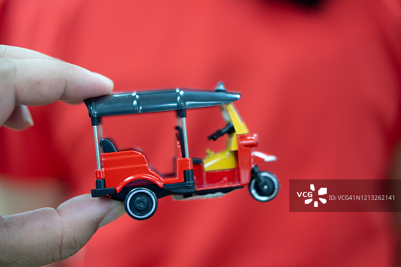 手持红色嘟嘟车玩具，象征泰国，红色背景图片素材