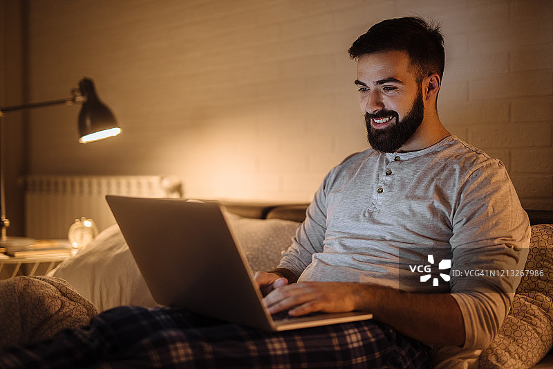 年轻男人在床上用笔记本电脑工作到深夜图片素材