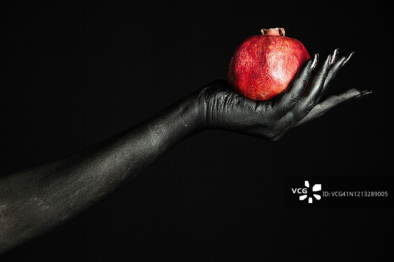 黑色颜料涂绘的女性手中的新鲜石榴图片素材