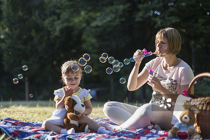在户外休息时为女儿吹肥皂泡的女人图片素材