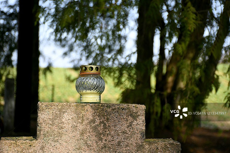 波兰，绿树成荫的墓地中央，纪念士兵的历史石十字架上，玻璃金属杯制成的祭祀蜡烛或守夜灯特写图片素材