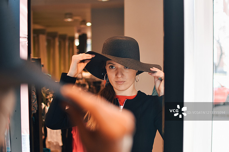 微笑的女人试戴新帽子，看着镜子里的倒影图片素材