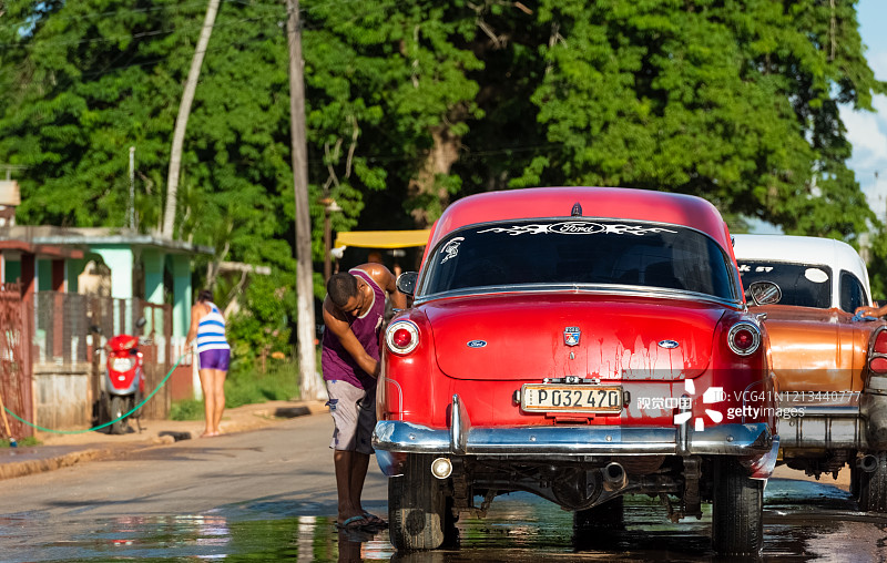 古巴男子在古巴基马多德吉内斯小镇清洗1953年红色福特老爷车图片素材