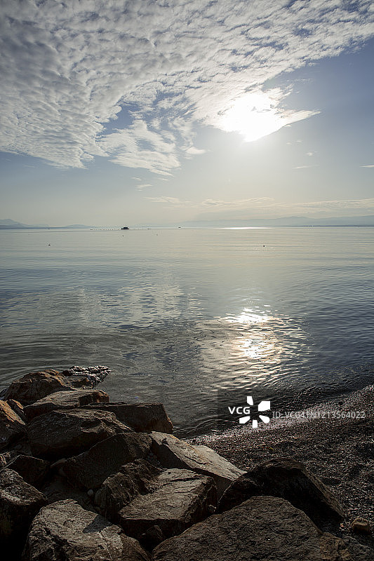 阳光倒映在岩石海滩后方清澈的湖水中图片素材