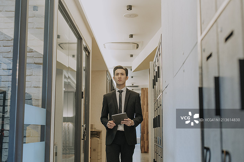 亚裔华人英俊男高管手持数字平板走在办公楼走廊里图片素材