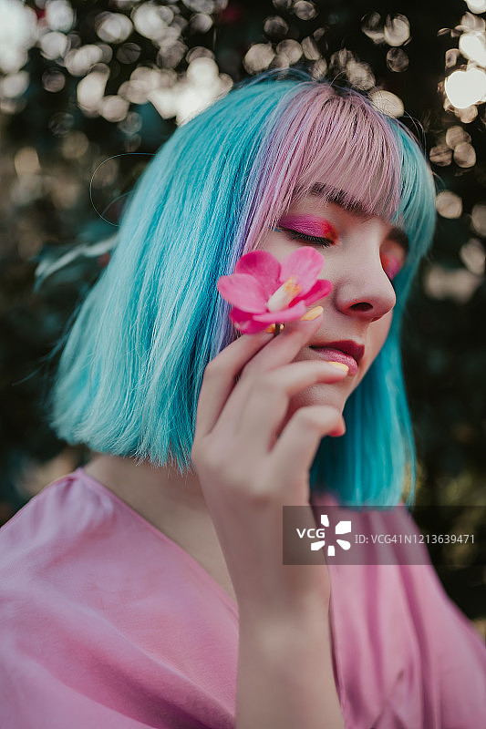 闭着眼睛手持樱花的蓝发年轻女子图片素材